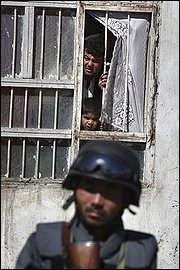 An Afghan man and boy look out form their window as an Afghan counter-terrorism officer stands guard in Kabul, Afghanistan, Wednesday, Aug. 19, 2009 where gun battles broke out between Afghan forces and three militants with AK-47 rifles and hand grenades who overran a bank. Police stormed the building and killed the three insurgents. (AP Photo/Rafiq Maqbool)